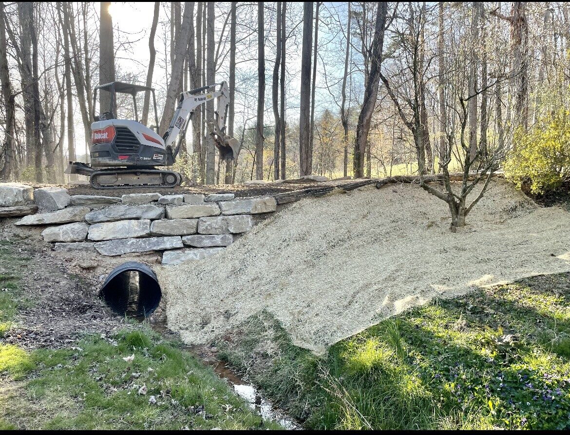 Stone retaining wall with drainage culvert and Bobcat excavator